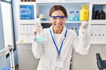 Young brunette woman working at scientist laboratory screaming proud, celebrating victory and success very excited with raised arm