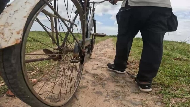 video angle from below, the spokes of a rotating bicycle wheel, and the footsteps of people guiding bicycles on the edge of the forest in Indonesia's Way Kambas National Park.