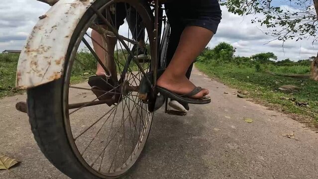 video angle from below, feet pedaling a bicycle and the spokes of a rotating bicycle wheel, walking along a road on the edge of the forest in Indonesia's Way Kambas National Park.