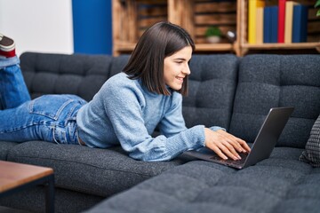 Young beautiful hispanic woman using laptop lying on sofa at home