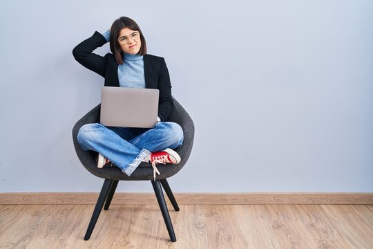 Young hispanic woman sitting on chair using computer laptop confuse and wondering about question. uncertain with doubt, thinking with hand on head. pensive concept.