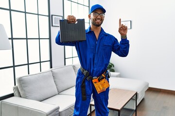 Young indian technician holding toolbox and screwdriver at house surprised with an idea or question pointing finger with happy face, number one