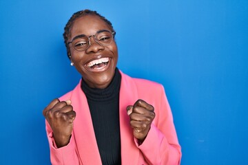 Beautiful black woman standing over blue background celebrating surprised and amazed for success with arms raised and open eyes. winner concept.