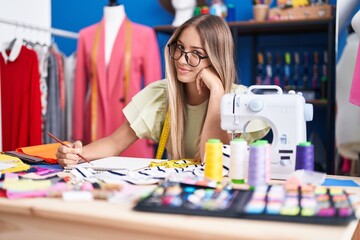 Fototapeta premium Young beautiful hispanic woman tailor smiling confident drawing on notebook at clothing factory