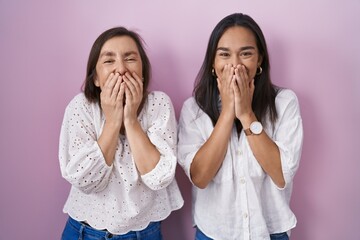 Hispanic mother and daughter together laughing and embarrassed giggle covering mouth with hands,...
