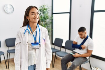 Young asian doctor woman at waiting room with a man with a broken arm looking away to side with smile on face, natural expression. laughing confident.