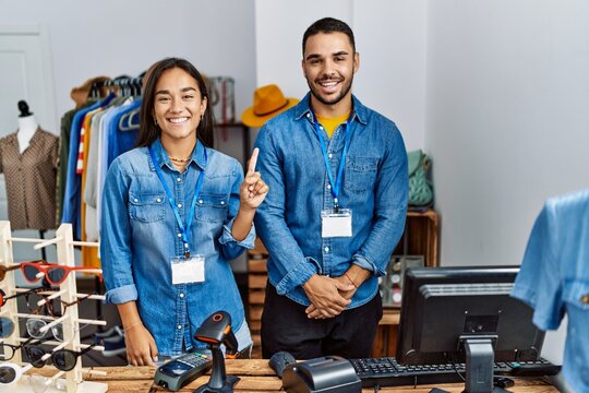 Young interracial people working at retail boutique showing and pointing up with finger number one while smiling confident and happy.