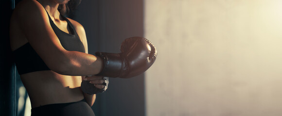 Close-up young woman wearing boxing glove in the gym.