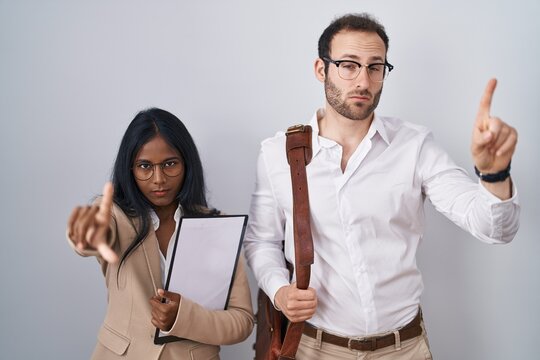 Interracial business couple wearing glasses pointing with finger up and angry expression, showing no gesture