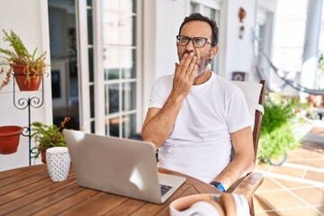 Middle age man using computer laptop at home bored yawning tired covering mouth with hand. restless and sleepiness.