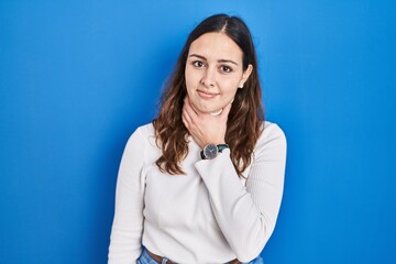 Young hispanic woman standing over blue background touching painful neck, sore throat for flu, clod and infection