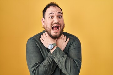 Plus size hispanic man with beard standing over yellow background shouting suffocate because painful strangle. health problem. asphyxiate and suicide concept.