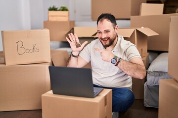 Plus size hispanic man with beard moving to a new home doing video call smiling happy pointing with hand and finger