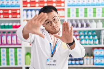 Chinese young man working at pharmacy drugstore doing frame using hands palms and fingers, camera perspective