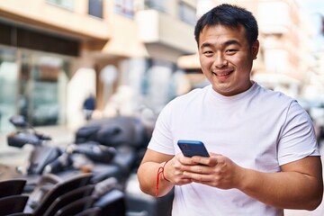 Young chinese man smiling confident using smartphone at street