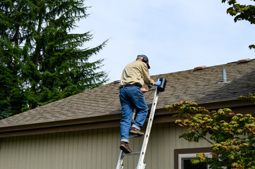 Fototapeta premium Senior man climbing an aluminum extension ladder to a home rooftop with a container of moss killer granules 