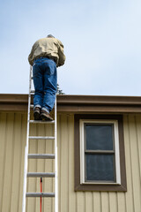 Fototapeta premium Senior man climbing an aluminum extension ladder to a home rooftop 