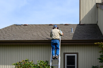 Fall maintenance, senior man climbing an extension ladder with a gas powered leaf blower to clean the roof of a residential house
