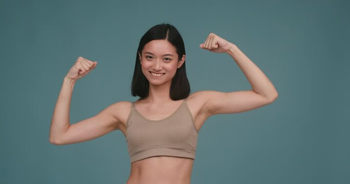 Sportive Asian woman raises hands to show arm muscles
