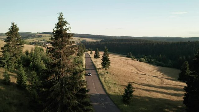 Aerial view of a single car driving towards the camera on an empty road on anice summer evening.