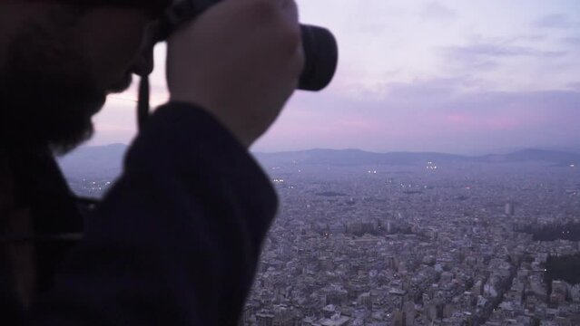 Young tourist man with hat taking a picture to the city in Athens at sunset in mount lycabettus