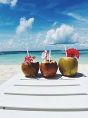 Tropical fresh coconut cocktail on white beach. Three coconut drinks at a luxury tropical resort in the Maldives. Fresh coconut cocktails on the sandy beach of Maldives with turquoise sea background.