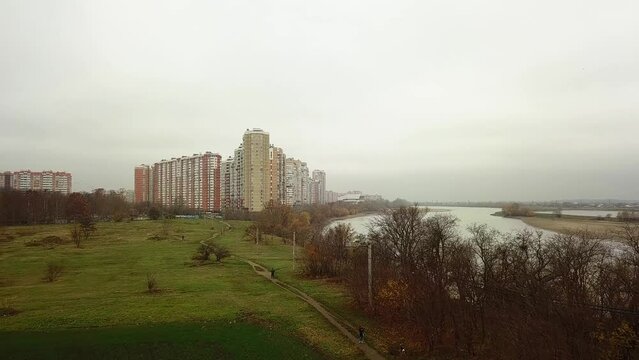 aerial view of a field and a wasteland on the outskirts of a large city with high-rise buildings of modern architecture near a wide river on an autumn cloudy and rainy day