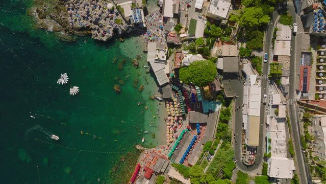 Top down panning shot of sea coast with beach and restaurants. Crystal clear turquoise water in tourist resort. Capri, Campania, Italy