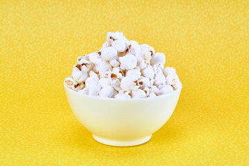 a white bowl of salted popcorn on a yellow background with copy space for advertising.