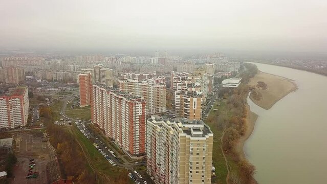 aerial view of a field and a wasteland on the outskirts of a large city with high-rise buildings of modern architecture near a wide river on an autumn cloudy and rainy day