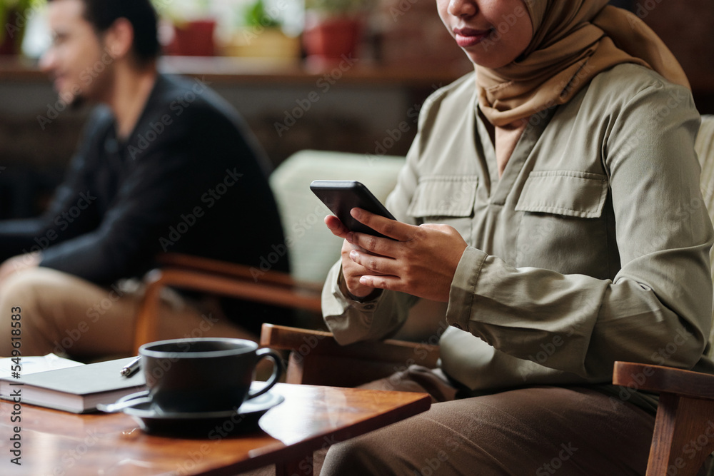 Aufkleber hands of young muslim female employee using smartphone while sitting by table with cup of tea and no