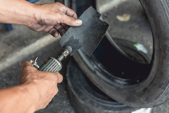 A man using an air die grinder with a sphere rotary burr to smoothen the surface of a piece of rubber to be used to cover a hole in a tire. Vulcanizing procedure.
