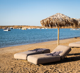 Photo of empty sun beds with thatched umbrella for rent on a beach on the Greek island of Paros.