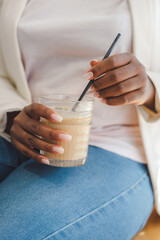 Hands of an African woman holding a cold drink with a straw. Businesswoman enjoys relaxing with glass of caffeine on coffee break for refreshment.