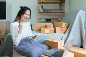 Starting small business entrepreneur of independent young Asian woman online seller is using computer and taking orders to pack products for delivery to customers. SME delivery concept