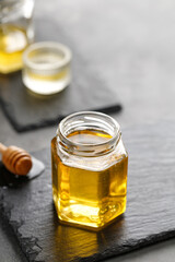 Glass jar of honey with wooden honey dipper, drizzler on a dark slate board and black background. Superfood, Alternative of sugar. Copy space, text.