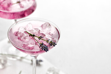 Lavender cocktail Purple drink in a glass on white board and white background with ice and lavender flowers. .Iced cold summer drink, lemonade.