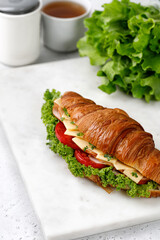 Fresh french croissant with cheese, tomatoes, lettuce on paper in the morning with cup of tea.