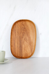 Wooden oval oak dish, board, tray standing near the wall. Empty wooden plate on kitchen white...