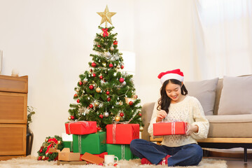 Fototapeta na wymiar Christmas concept, Asian woman sitting in christmas decorated living room and open christmas gift
