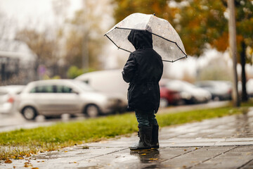 A rejected little boy is standing on the rainy weather all alone with his umbrella.