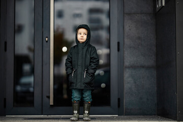 A sad rejected foster child is standing on the rain and waiting for his parents.