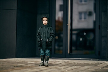 A rejected little boy is standing on the rain left alone.