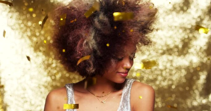 Black woman, afro and dancing in falling confetti in gold studio background, dance night club or party event location. Slow motion, fashion and person with alcohol champagne glass in new years disco
