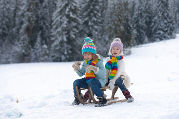 Kids boy and little girl enjoying a sleigh ride. Children sibling together sledding, play outdoors in snow on mountains in winter. New Year wallpaper, Christmas greeting card.