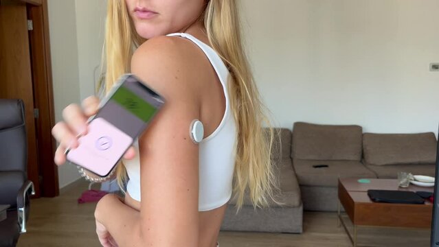 Woman checking blood sugar level with the glucometer device on her shoulder with an app