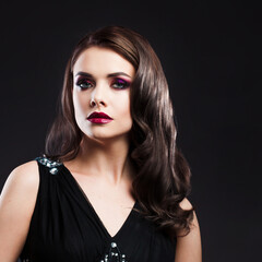 Fototapeta premium Portrait of a young luxurious woman in a low key. Bright makeup with scarlet lipstick, hairstyle with curls, portrait on a black background