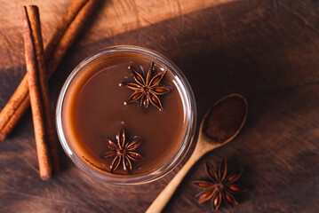 Hot cocoa in cup glass with cinnamon stick, star anise and cocoa powder on wooden background, Hot drink in winter season, Table top view