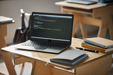Close-up of laptop with codes on monitor standing on desk in class during IT lesson