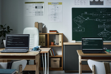 Horizontal image of modern empty class with computers with coding on monitors for IT lesson